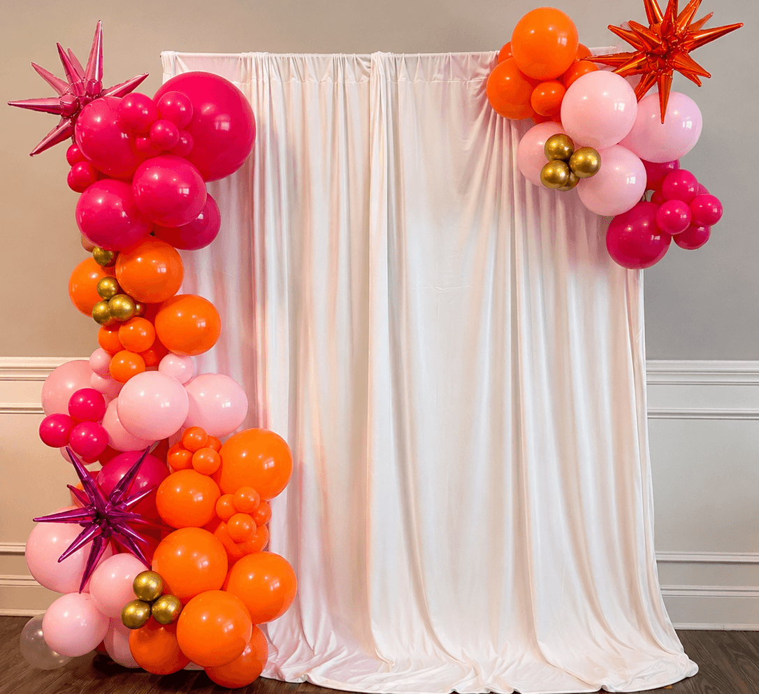 Hot pink, orange, and gold balloon arch with starburst accents